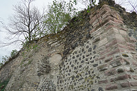 Westecke der Grabenmauer aus Buckelquadern, mittig Rundbogen einer  Zwischenmauer, links davon hinter dem Strebepfeiler vorstehendes Kernmauerwerk, rechts oben ausgewaschene Mauerstruktur der Grabmauer / Stadtmauer in 79206 Breisach, Breisach am Rhein (12.2021 - S. King)